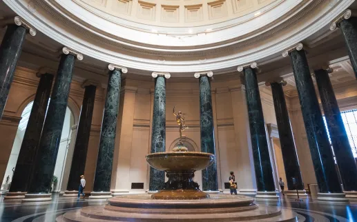 Grand rotunda of the National Gallery of Art featuring a circular fountain and towering marble columns.
